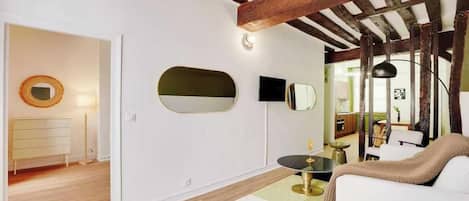 Una sala de estar moderna con un sofá blanco, un espejo redondo, un televisor de pantalla plana y una pequeña mesa redonda.