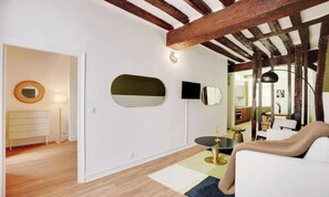 Una sala de estar moderna con un sofá blanco, un espejo redondo, un televisor de pantalla plana y una pequeña mesa redonda.