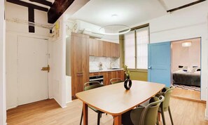 Cocina compacta con armarios de madera, comedor con mesa y sillas, y un dormitorio con cama y mesita de noche.