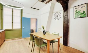 A dining area with a wooden table and chairs, a clock on the wall, and a framed plant life poster. - AN IDEAL BASE FOR EXPERIENCING THE VERY BEST OF THE FRENCH CAPITAL-SAINT GERMAIN (Paris)
