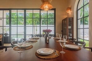 A dining table set for six with a view of a lush garden through large windows. - 10-bedroom- all Suites - Wellness Compound - Private Sauna/Ice Bath/Yoga Deck (Tulum)