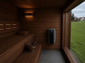 A sauna room with wooden walls, a bench, a bucket, and a sauna mat. - Chalet Scandi – Sauna & Mountain Views Near Kufstein (Ebbs)
