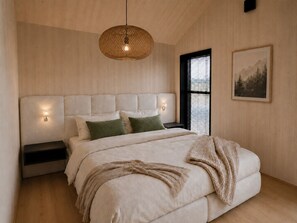A bedroom with a large bed, a hanging light fixture, a nightstand, a window with blinds, and a framed picture on the wall. - Chalet Scandi – Sauna & Mountain Views Near Kufstein (Ebbs)
