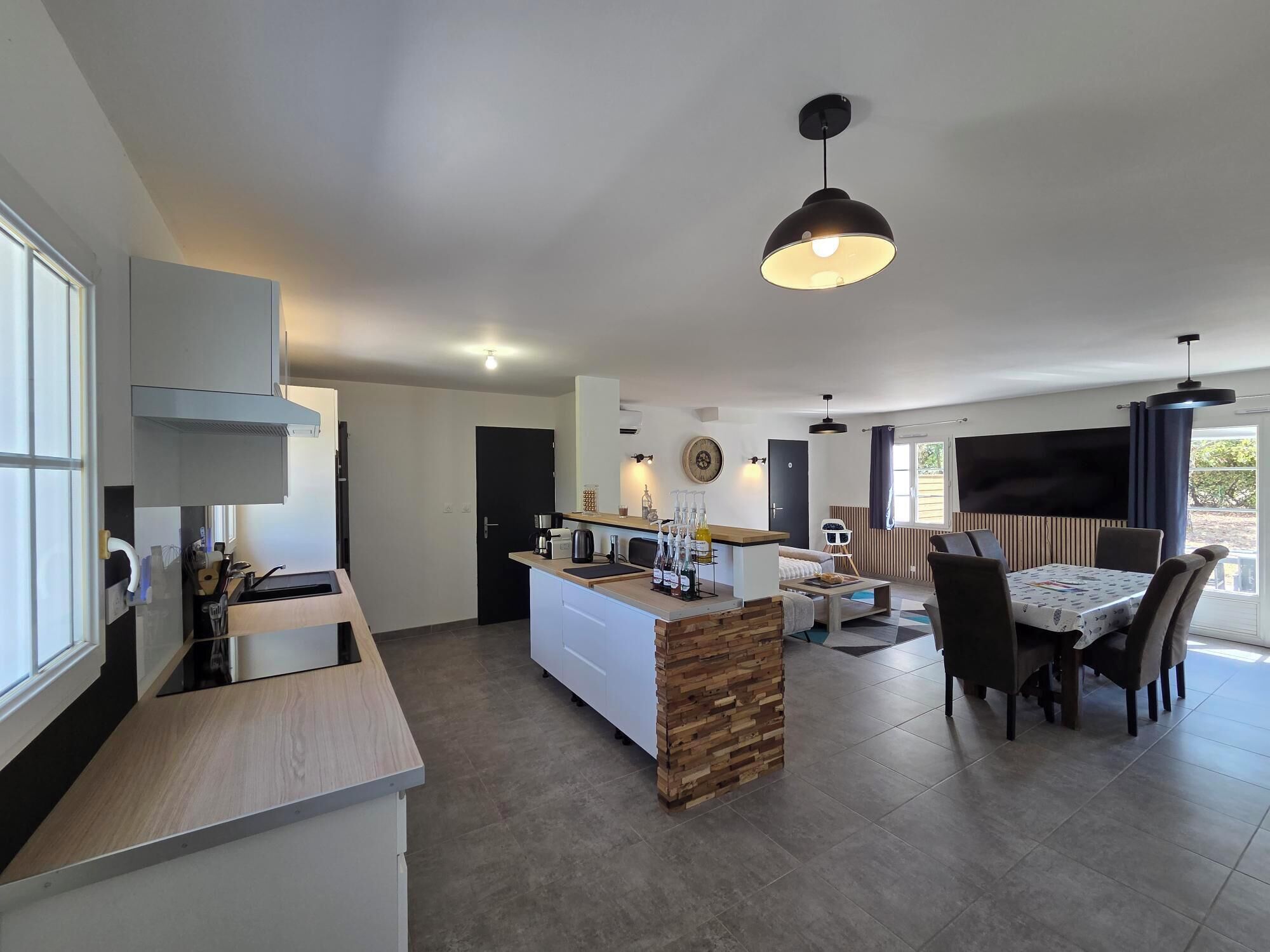 A modern kitchen with a central island, a dining area with a table and chairs, and a living space with a sofa and TV.