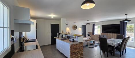 A modern kitchen with a central island, a dining area with a table and chairs, and a living space with a sofa and TV.