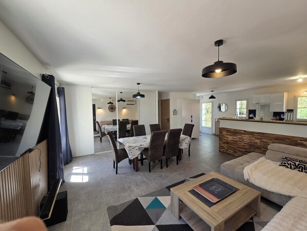 A modern living room with a sofa, a coffee table, and a dining area with chairs and a table. - Vrbo Property (La Jonchère)