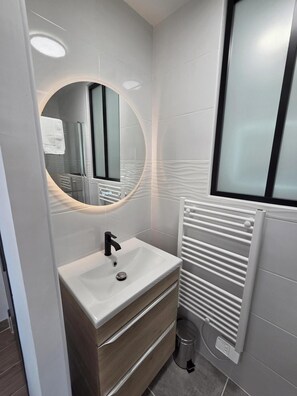 A modern bathroom with a white sink, a round mirror, and a window. - Vrbo Property (La Jonchère)