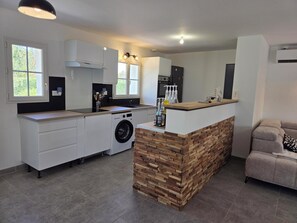A modern kitchen with a built-in washing machine, a wooden island, and a seating area with a sofa. - Vrbo Property (La Jonchère)