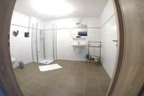 A bathroom with a shower, toilet, sink, and a small shelf with items. - Country House Dream View (Ofterschwang)