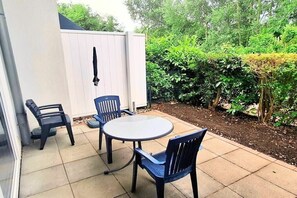 Un patio exterior con una mesa redonda y cuatro sillas, rodeado por una cerca blanca y abundante follaje.