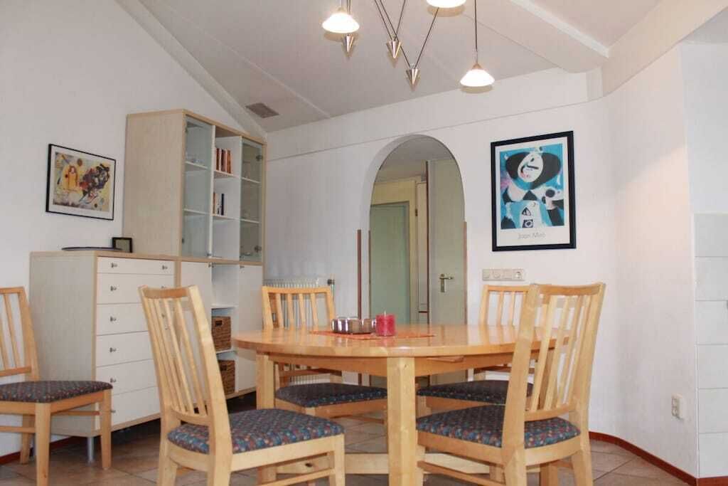 A dining area with a wooden table and chairs, a bookshelf, and a framed artwork on the wall.