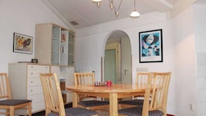 Uma área de refeições com uma mesa e cadeiras de madeira, uma estante de livros e uma obra de arte emoldurada na parede.