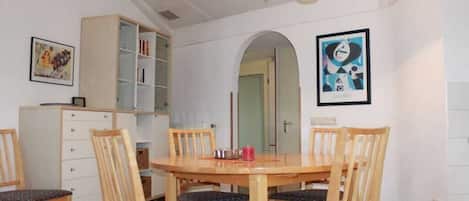 Un comedor con mesa y sillas de madera, una estantería y una obra de arte enmarcada en la pared.