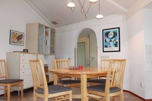A dining area with a wooden table and chairs, a bookshelf, and a framed artwork on the wall. - Bungalow with 2 bedrooms (Julianadorp aan zee)