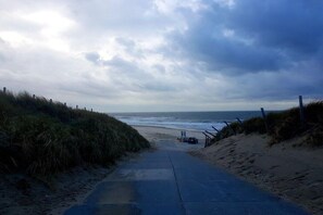 A pathway leading to the beach with a fence on one side and a parked car on the other. - Bungalow with 2 bedrooms (Julianadorp aan zee)