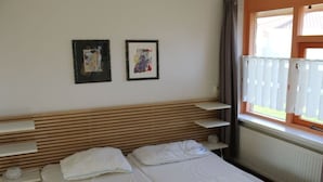 Quarto de hotel com cabeceira de madeira, duas camas, janela com persianas e duas fotografias emolduradas na parede.