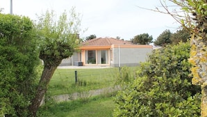 Edifício residencial com telhado ladrilhado, quintal cercado e vegetação ao redor.