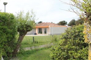 A residential building with a tiled roof, a fenced yard, and surrounding greenery. - Bungalow with 2 bedrooms (Julianadorp aan zee)