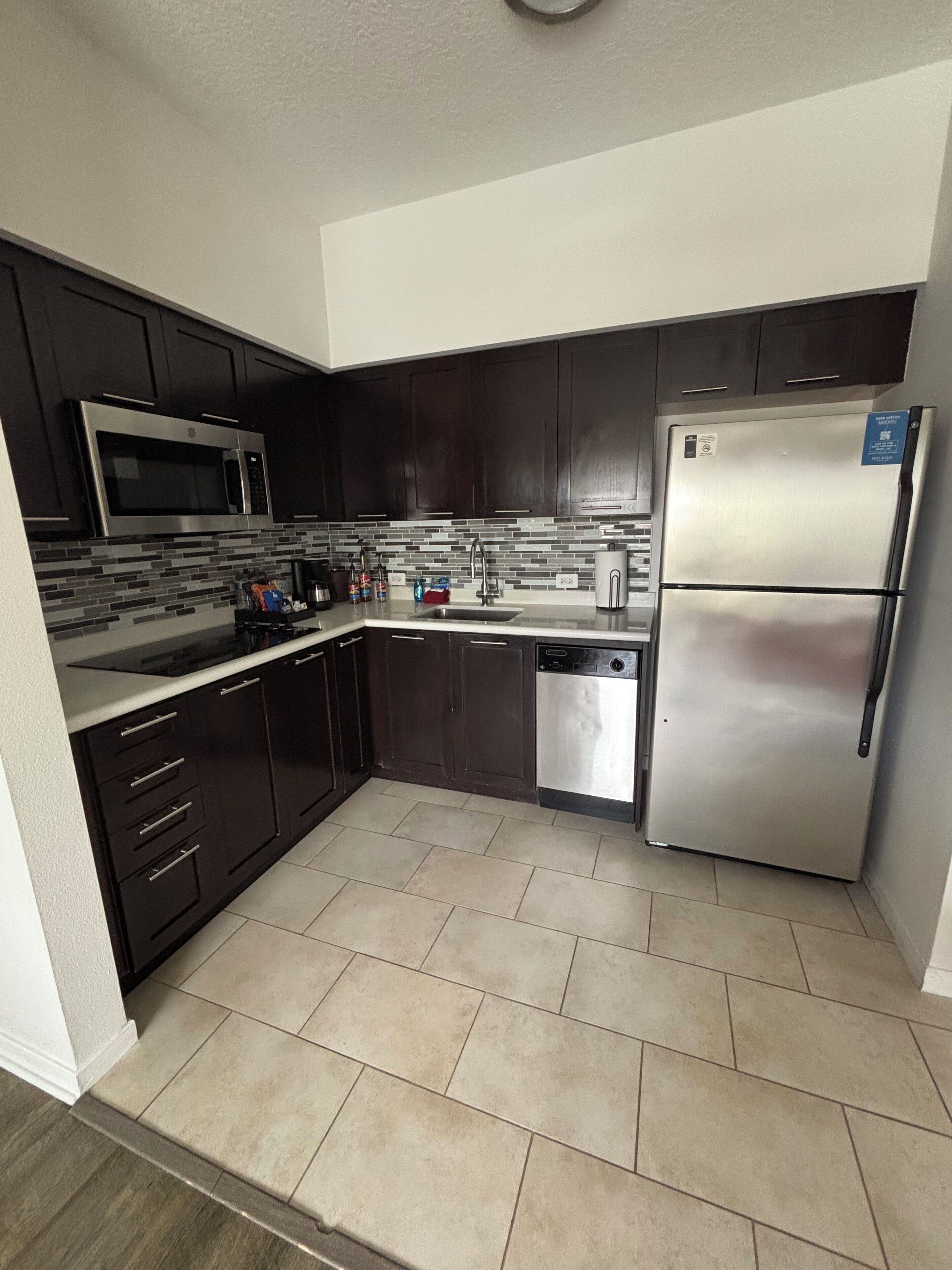 A modern kitchen with dark cabinetry, a stainless steel refrigerator, a microwave, and a dishwasher.