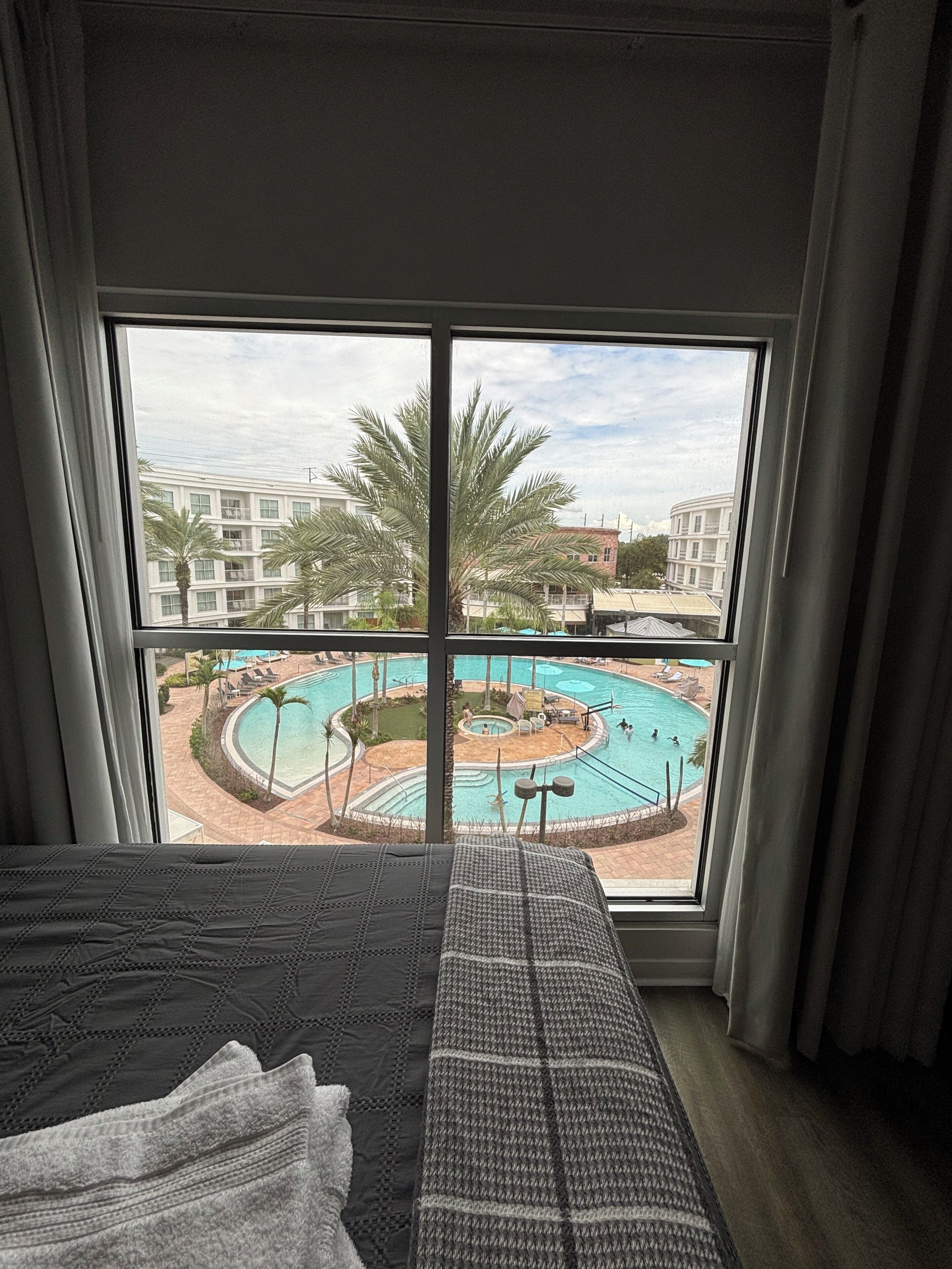 Ein Hotelzimmer mit großem Fenster mit Blick auf einen Swimmingpool und Palmen.