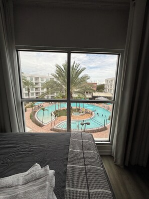 Een hotelkamer met een groot raam met uitzicht op een zwembad en palmbomen.