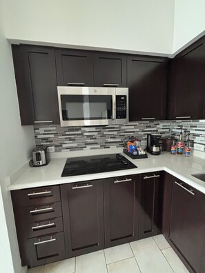 A modern kitchen with dark cabinets, a stainless steel microwave, a black induction cooktop, and a tiled backsplash. - Charming 2-bedroom apartment at MELIA
CELEBRATION 
No resort fee
Free Shuttle  (Kissimmee)
