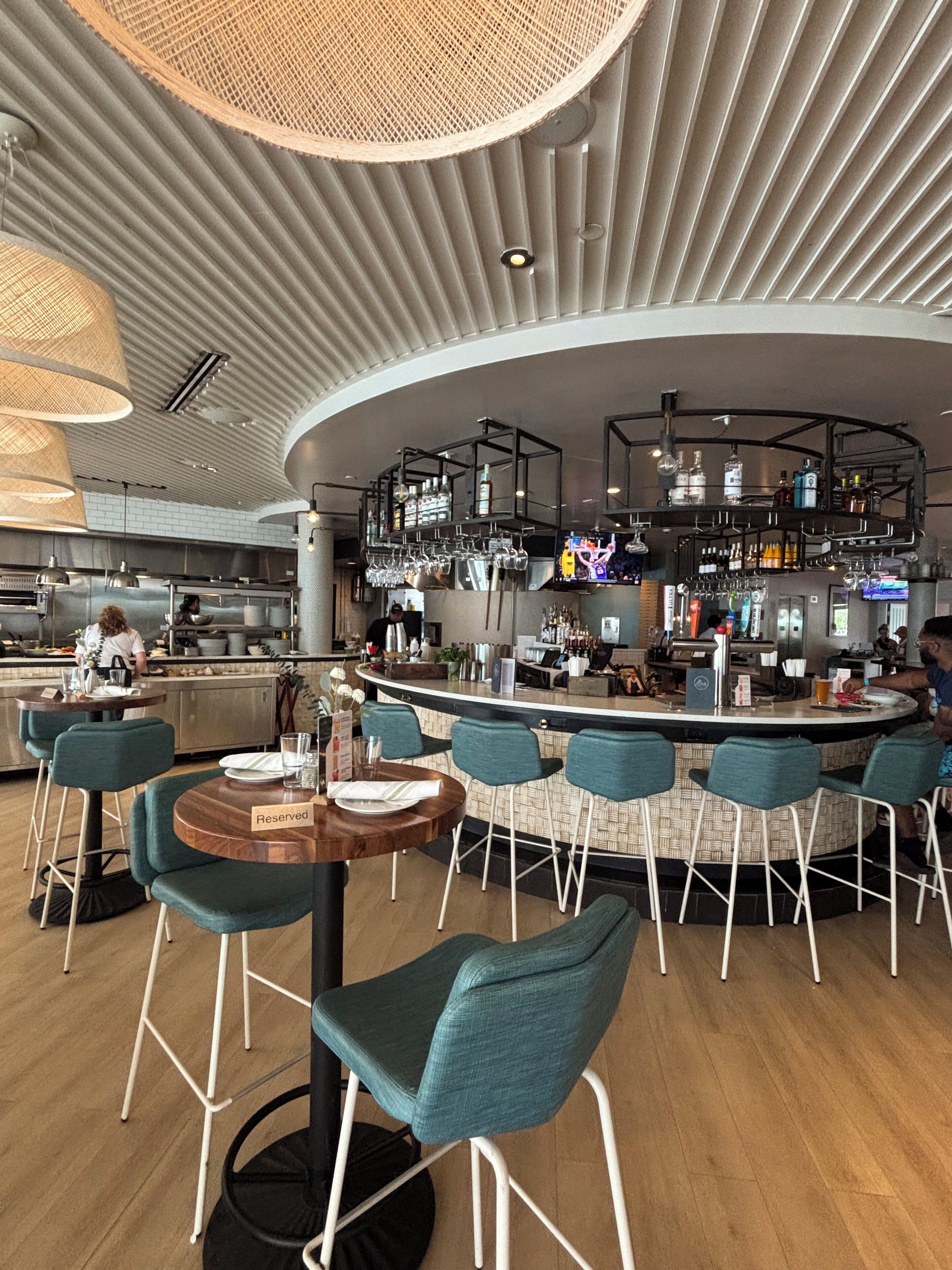 A modern bar area with a curved counter, bar stools, and a seating area with tables and chairs.