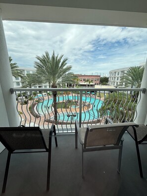 A balcony with two chairs, overlooking a pool area with palm trees and buildings in the background. - Charming 2-bedroom apartment at MELIA
CELEBRATION 
No resort fee
Free Shuttle  (Kissimmee)