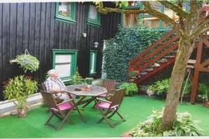 Een houten huis met een trap, een ronde tafel met stoelen en potplanten.