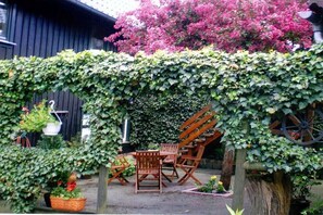 Un jardin agrémenté d’une pergola en bois recouverte de lierre, de meubles d’extérieur et d’une brouette.