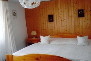 Een slaapkamer met houten lambrisering, een bed, twee kussens, een nachtkastje en een wandlamp.