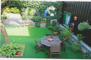 Een terras met een ronde tafel en stoelen, omringd door potplanten en een houten hek.