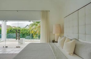Ein Schlafzimmer mit einem großen Bett, einem Nachttisch, einer Lampe und Blick auf Grünflächen.