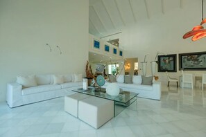 Ein modernes Wohnzimmer mit einem Glastisch, weißen Sofas und einem Essbereich mit weißen Stühlen.