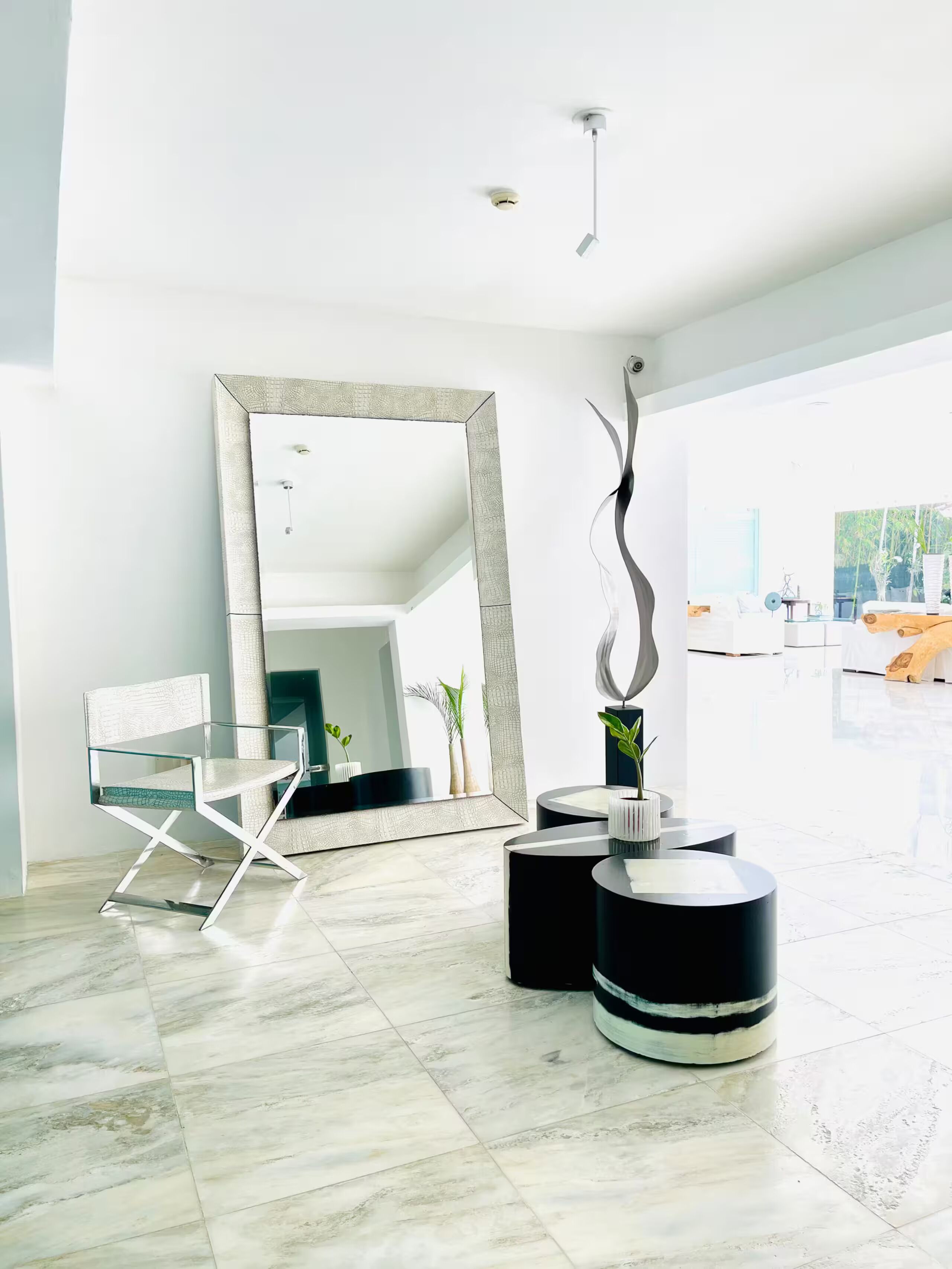 Un intérieur moderne avec une chaise en verre, un grand miroir et une œuvre sculpturale.
