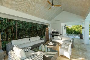 Un espacio al aire libre moderno con ventilador de techo, sofá, mesa de comedor y parrilla.