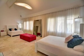 Ein Hotelzimmer mit einem Bett, einem roten Hocker, einem weißen Sofa, einem Spiegel und einem Fenster mit Vorhängen.