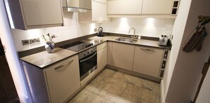 A compact kitchen with a stove, oven, sink, and a kettle. - Pegasus Cottage - North East Escapes (Craster)
