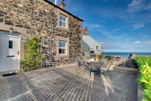 Ein Steinhaus mit einer Terrasse, die einen Tisch, Stühle und Blick auf das Meer bietet.
