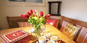 Ein Esstisch mit einer Vase roter Tulpen, einer Schachtel Schokoladenkekse und mehreren weißen Tassen.
