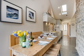 A dining area with a wooden table set for a meal, a vase of flowers, and wine bottles. - Harbour Masters House - North East Escapes (Craster)