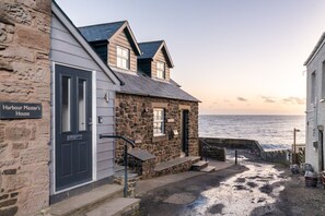 Ein Steinhaus mit einem Schild, auf dem 'Harbour Master's House' steht, einer Treppe, die zu einer Tür führt, und Blick auf das Meer.
