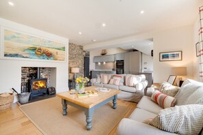 A cozy living room with a fireplace, a sofa, a coffee table, and a painting on the wall. - Harbour Masters House - North East Escapes (Craster)