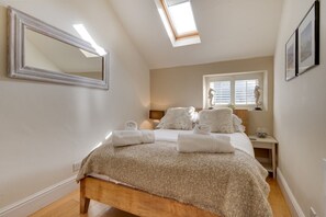 Ein Schlafzimmer mit Dachfenster, einem Bett mit einer flauschigen Decke, einem Nachttisch mit Lampe und einem Fenster mit Rollläden.