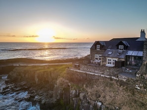 A coastal house with a stone facade, large windows, and a balcony overlooking the sea. - Harbour Masters House - North East Escapes (Craster)