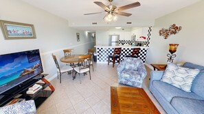 Uma sala de estar com televisão, sofá, mesa de centro e um espaço de jantar com cadeiras e mesa.