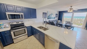 A modern kitchen with dark blue cabinets, stainless steel appliances, and a large island with a sink. - Pelican Isle 106 1 Bedroom Condo (Fort Walton Beach)