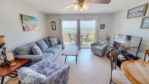 Una sala de estar con sofá, sillones, mesa de centro, televisor y balcón con vistas.