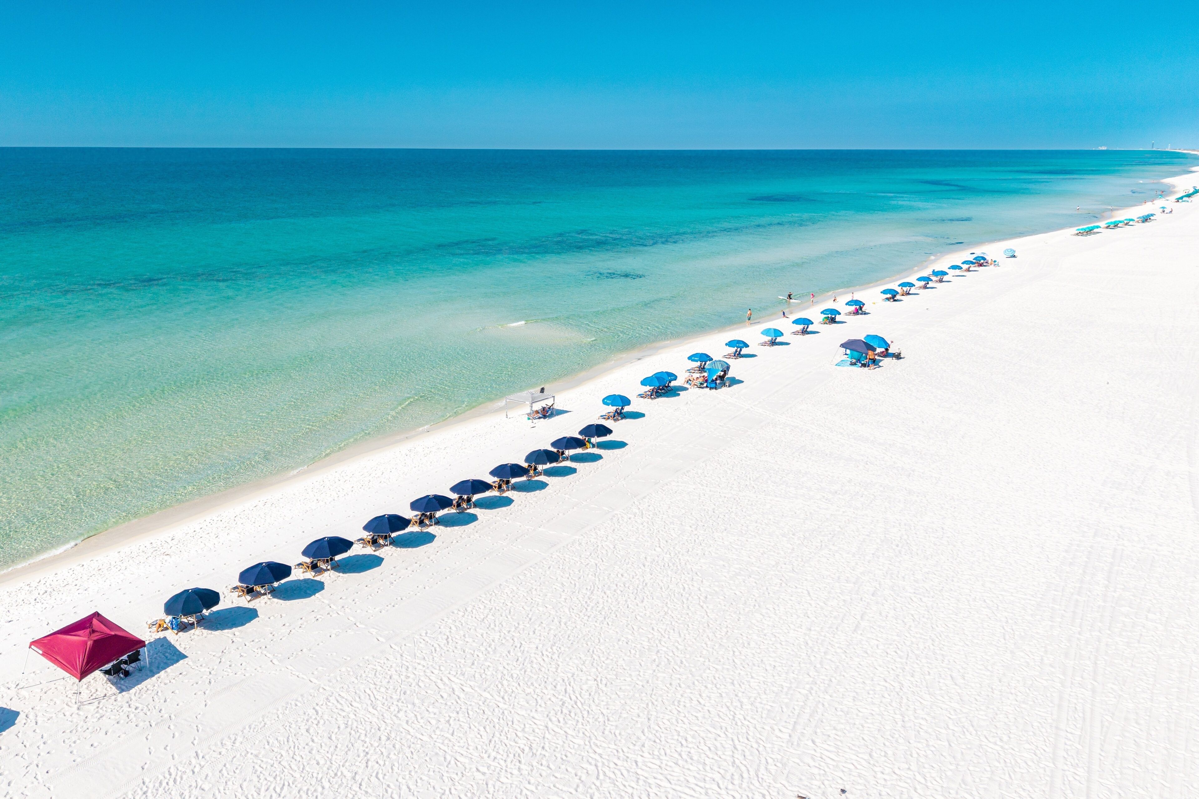 A beach with a row of blue umbrellas and a red umbrella on the sand.