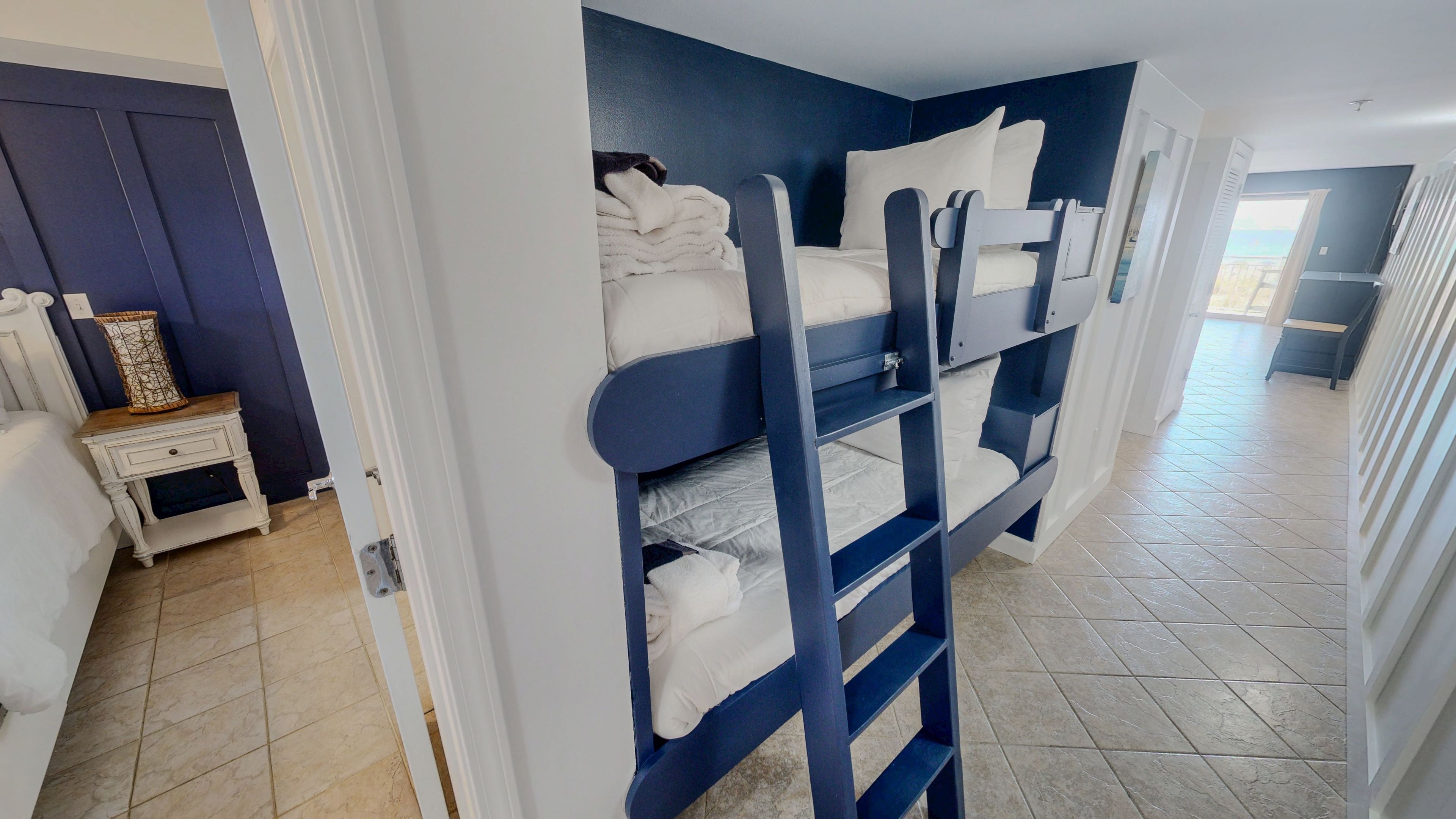 A room with a bunk bed, a bedside table with a lamp, and a view of the outside.